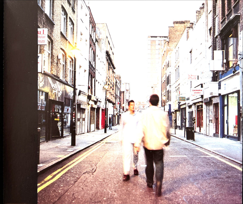 a couple of people walking down a street next to tall buildings